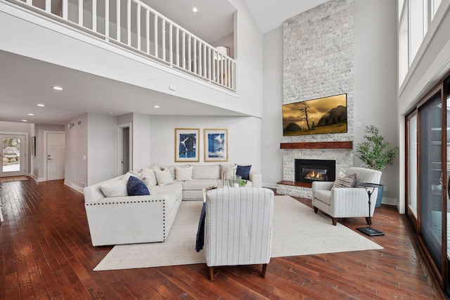 living room with dark hardwood / wood-style floors, a stone fireplace, and a high ceiling