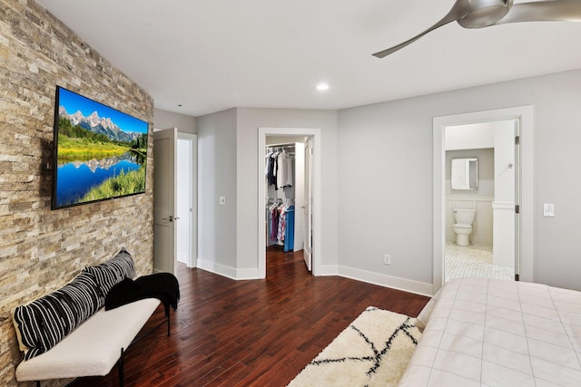 bedroom with connected bathroom, a walk in closet, a closet, hardwood / wood-style flooring, and ceiling fan