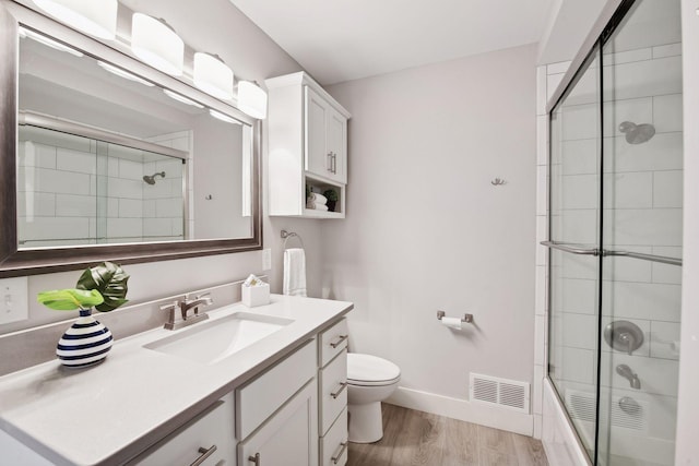 full bathroom featuring hardwood / wood-style flooring, vanity, combined bath / shower with glass door, and toilet