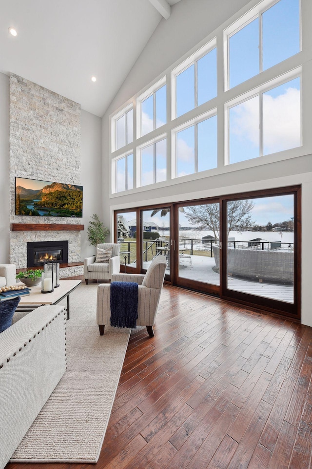 living room with beamed ceiling, a stone fireplace, dark wood-type flooring, and high vaulted ceiling