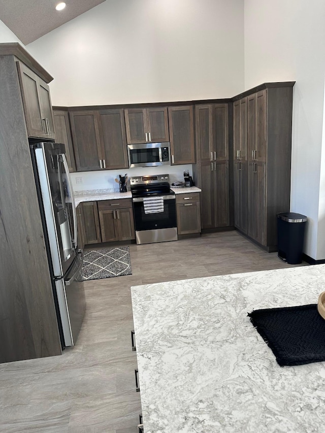 kitchen with high vaulted ceiling, appliances with stainless steel finishes, dark brown cabinetry, and light hardwood / wood-style floors