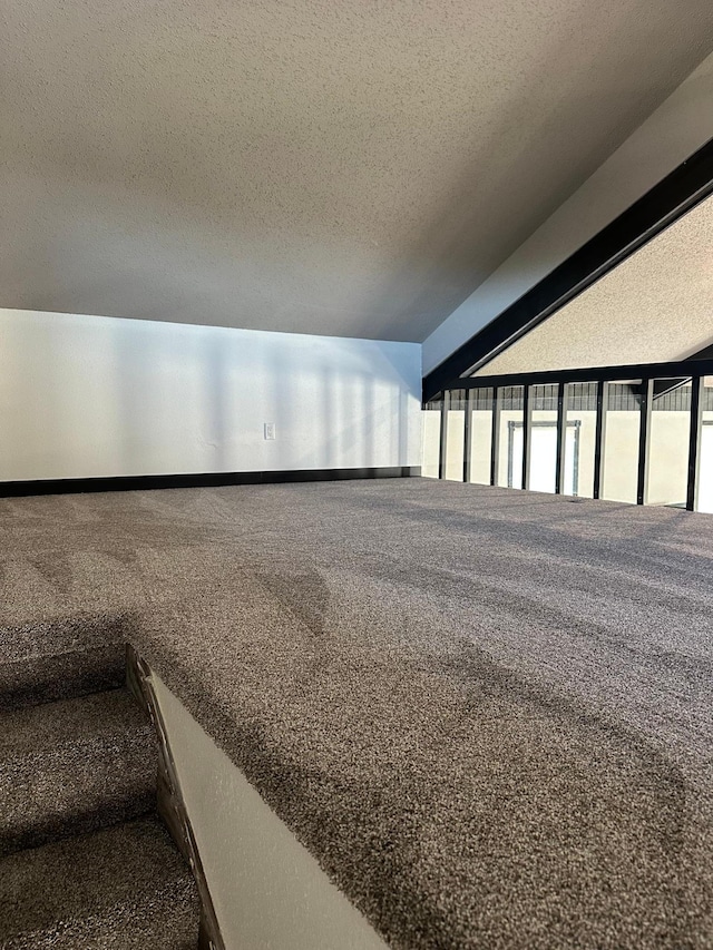 carpeted spare room featuring lofted ceiling with beams and a textured ceiling