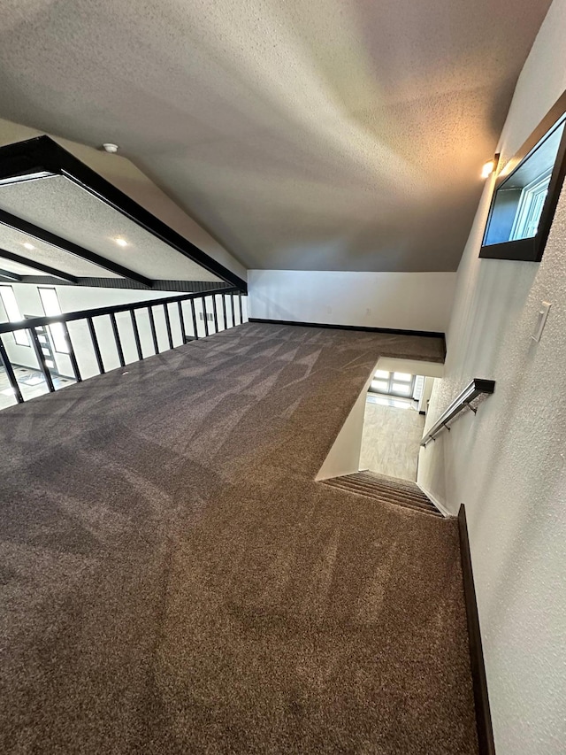 stairs with lofted ceiling with beams, a textured ceiling, and carpet floors