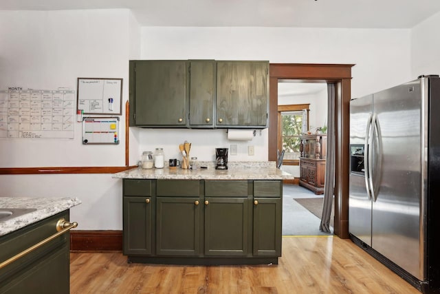 kitchen featuring green cabinets, stainless steel fridge, light stone countertops, and light wood-type flooring