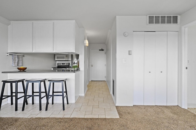 kitchen featuring white cabinets, stove, a breakfast bar area, and light carpet