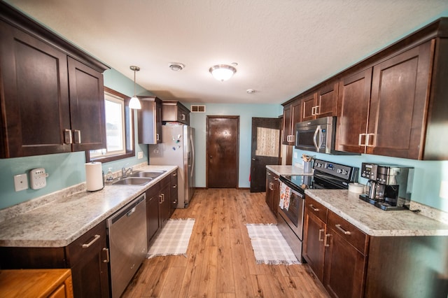 kitchen with dark brown cabinetry, sink, hanging light fixtures, appliances with stainless steel finishes, and light hardwood / wood-style floors