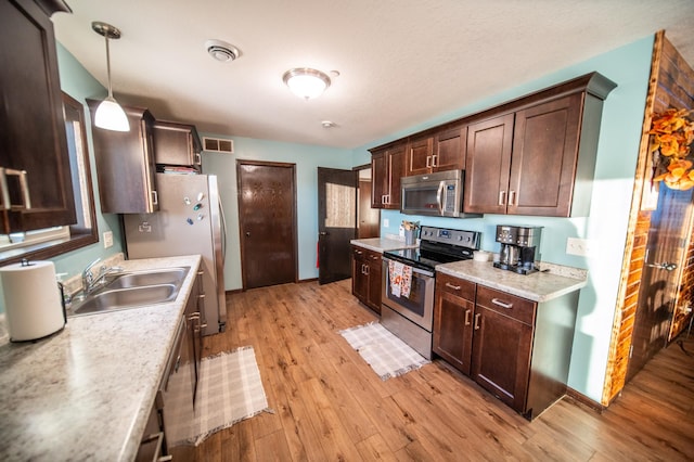 kitchen featuring sink, light hardwood / wood-style floors, hanging light fixtures, and appliances with stainless steel finishes