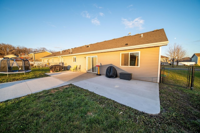 rear view of property featuring a trampoline, a yard, and a patio area