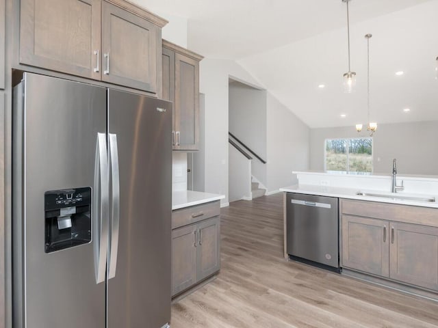 kitchen featuring lofted ceiling, light hardwood / wood-style flooring, sink, pendant lighting, and appliances with stainless steel finishes