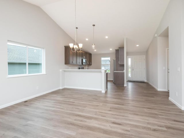 kitchen featuring light hardwood / wood-style floors, an inviting chandelier, kitchen peninsula, dark brown cabinets, and pendant lighting