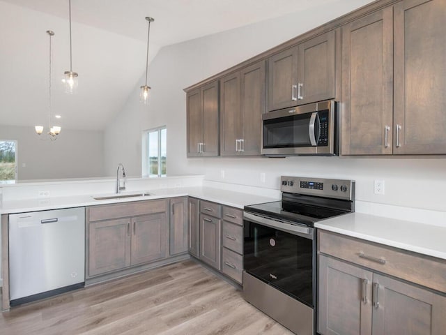 kitchen with stainless steel appliances, light wood-type flooring, pendant lighting, sink, and lofted ceiling