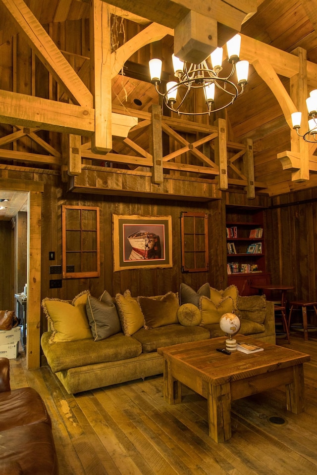 living room with hardwood / wood-style floors, wooden walls, a chandelier, and high vaulted ceiling