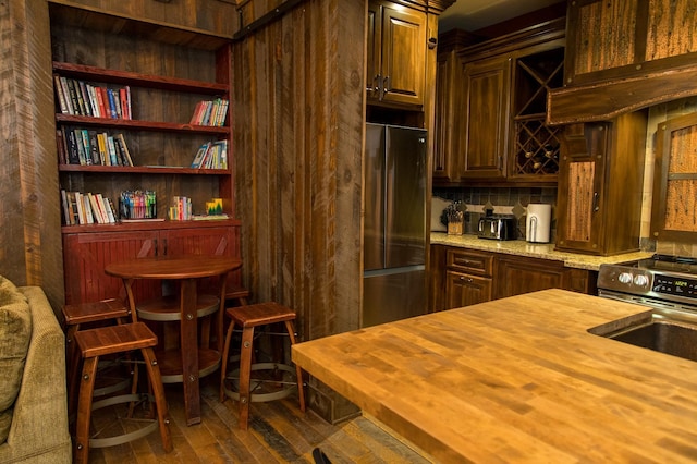 kitchen with dark hardwood / wood-style flooring, light stone counters, decorative backsplash, sink, and stainless steel fridge