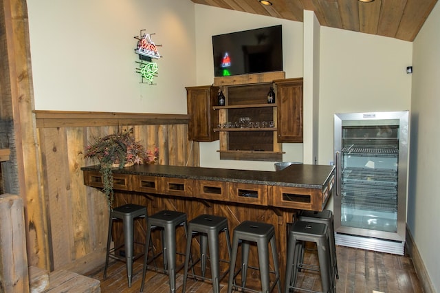 bar with wooden ceiling, wood walls, wine cooler, dark wood-type flooring, and vaulted ceiling