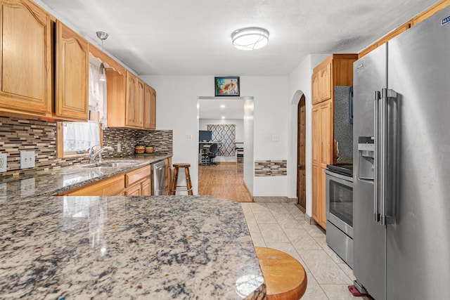 kitchen with dark stone counters, decorative backsplash, sink, appliances with stainless steel finishes, and decorative light fixtures