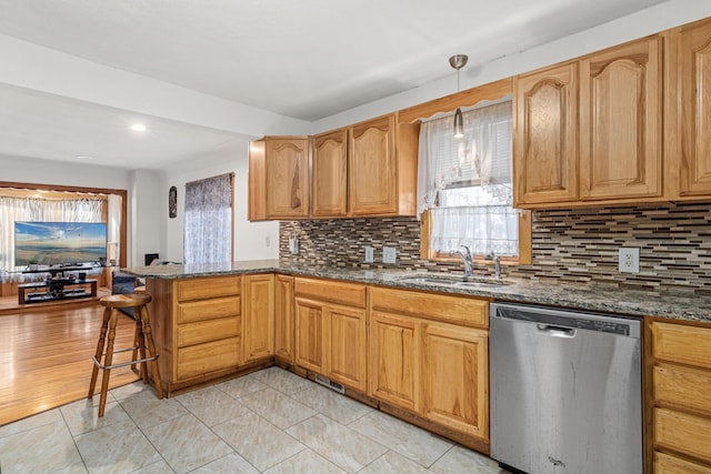 kitchen featuring dark stone counters, kitchen peninsula, sink, stainless steel dishwasher, and decorative light fixtures