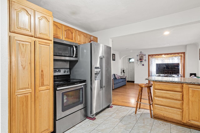 kitchen featuring a breakfast bar, stone counters, light hardwood / wood-style floors, and stainless steel appliances