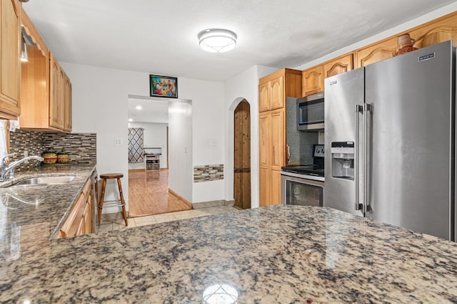 kitchen featuring tasteful backsplash, stainless steel appliances, light tile patterned floors, sink, and dark stone countertops