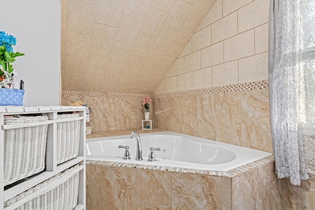 bathroom with vaulted ceiling, tile walls, and tiled tub