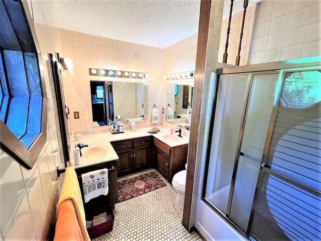 full bathroom with tile patterned floors, a textured ceiling, toilet, shower / bath combination with glass door, and tile walls