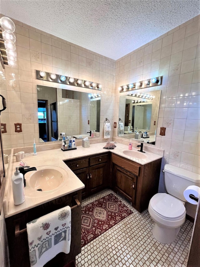 bathroom featuring tile patterned floors, a textured ceiling, toilet, vanity, and tile walls