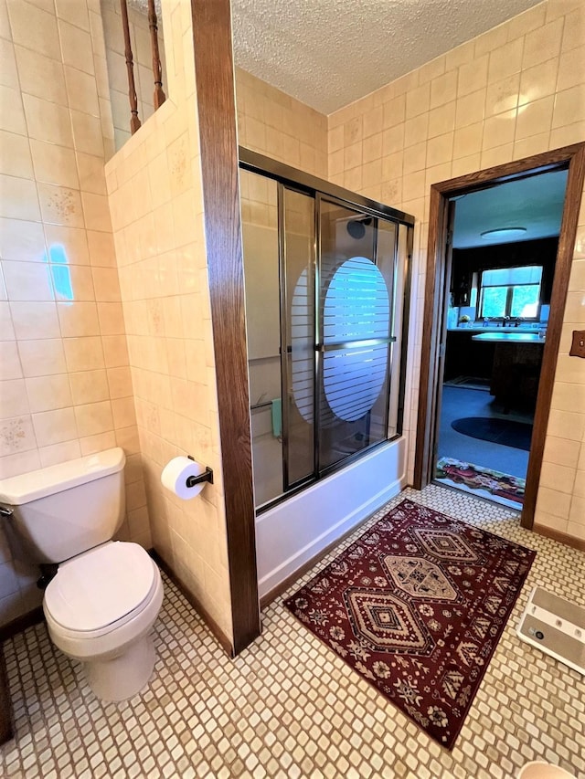 bathroom featuring shower / bath combination with glass door, a textured ceiling, tile walls, and toilet