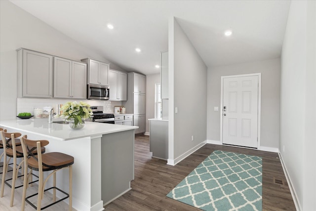 kitchen featuring stainless steel appliances, a breakfast bar, kitchen peninsula, lofted ceiling, and gray cabinetry