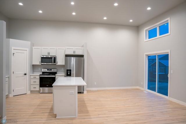 kitchen with stainless steel appliances, light hardwood / wood-style floors, a high ceiling, and white cabinetry