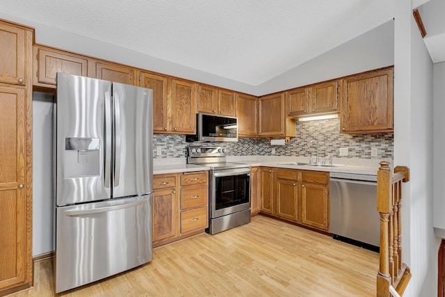 kitchen featuring sink, stainless steel appliances, light hardwood / wood-style flooring, backsplash, and vaulted ceiling