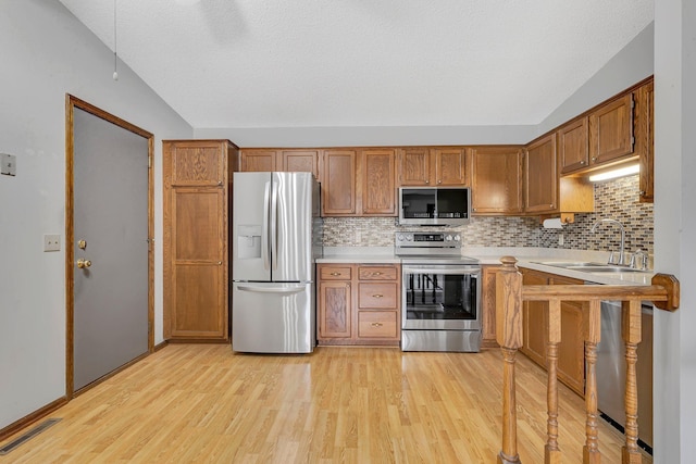 kitchen with appliances with stainless steel finishes, tasteful backsplash, vaulted ceiling, sink, and light hardwood / wood-style floors