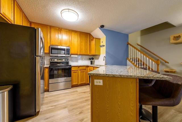 kitchen featuring stainless steel appliances, light hardwood / wood-style floors, light stone counters, kitchen peninsula, and a breakfast bar area