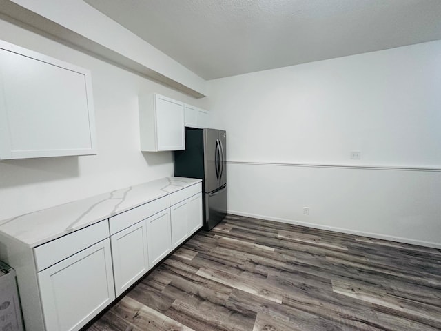 kitchen with white cabinets, stainless steel refrigerator, light stone countertops, and dark wood-type flooring