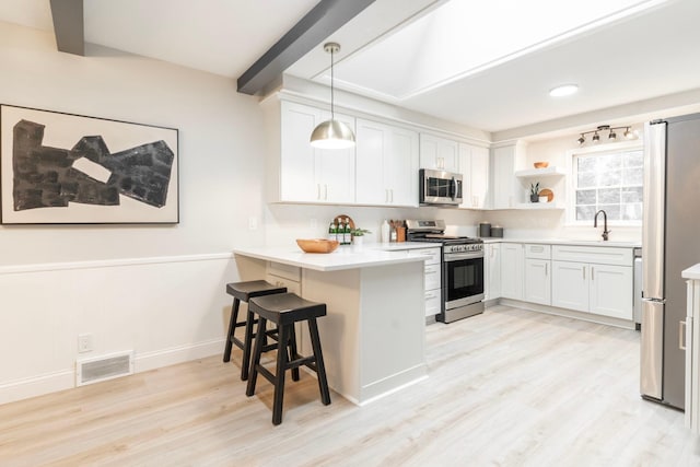 kitchen featuring stainless steel appliances, kitchen peninsula, hanging light fixtures, a kitchen breakfast bar, and white cabinetry