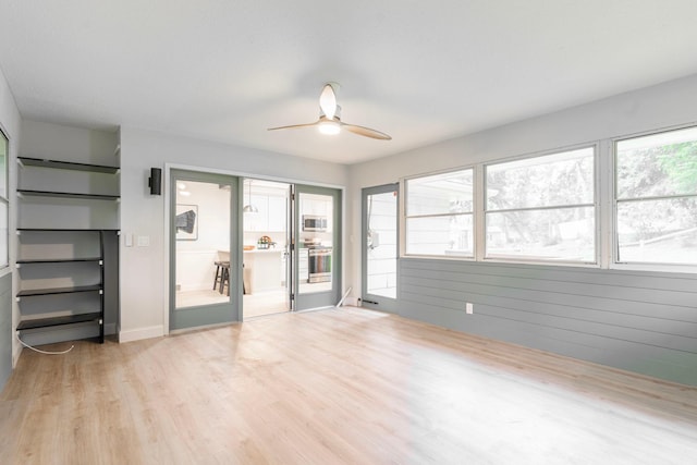 interior space with ceiling fan, wooden walls, light hardwood / wood-style floors, and plenty of natural light