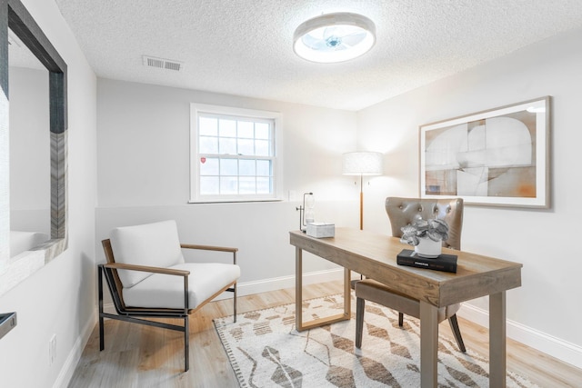 office with light wood-type flooring and a textured ceiling