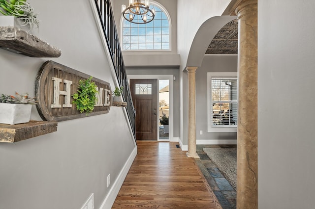 foyer entrance featuring a towering ceiling, ornate columns, a wealth of natural light, and wood finished floors