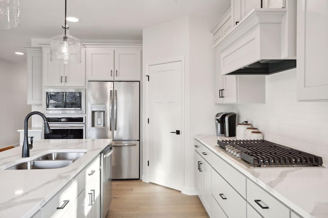 kitchen with white cabinetry, sink, stainless steel appliances, pendant lighting, and custom range hood