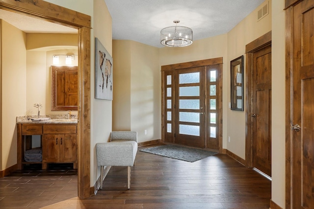 entryway with dark wood-type flooring, a chandelier, and a textured ceiling