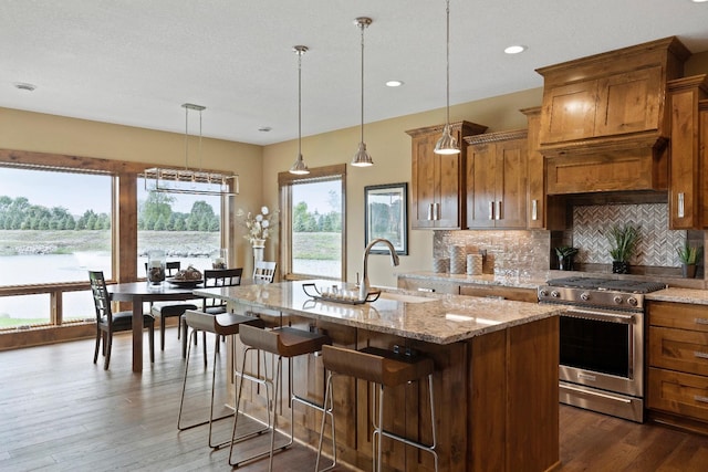 kitchen with stainless steel gas range, a center island with sink, sink, decorative light fixtures, and dark wood-type flooring