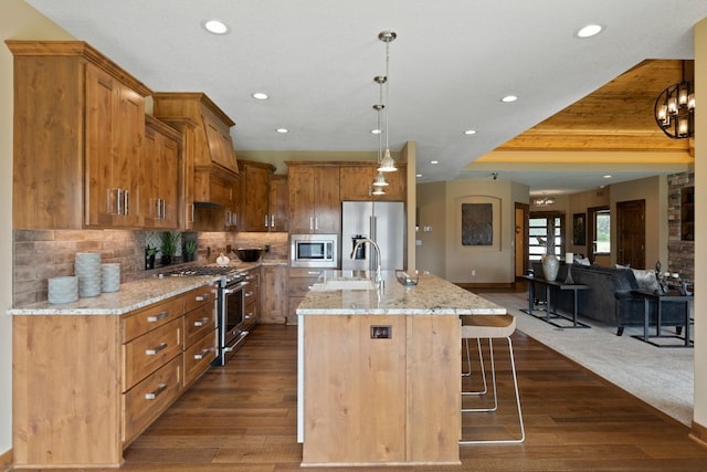 kitchen with a kitchen bar, stainless steel appliances, dark wood-type flooring, a center island with sink, and pendant lighting