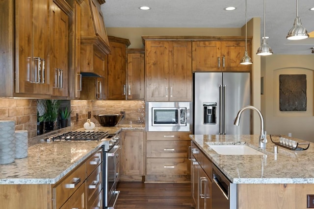 kitchen featuring dark wood-type flooring, sink, high quality appliances, light stone countertops, and pendant lighting