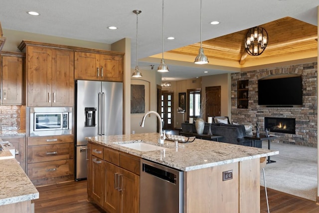 kitchen featuring sink, light stone counters, appliances with stainless steel finishes, an island with sink, and pendant lighting