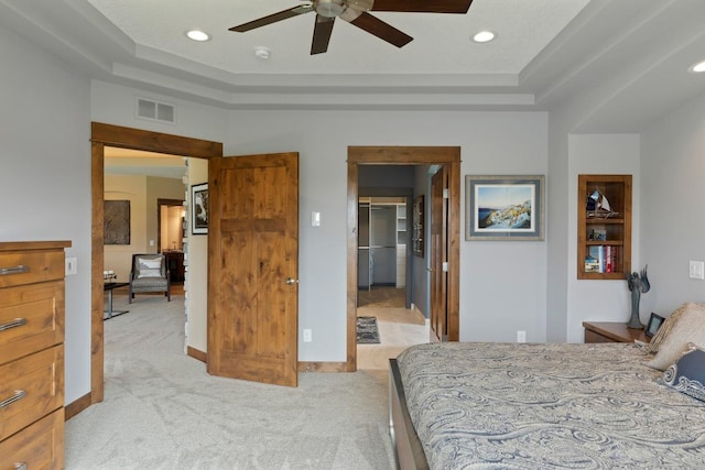 bedroom featuring a spacious closet, light colored carpet, ceiling fan, and a raised ceiling