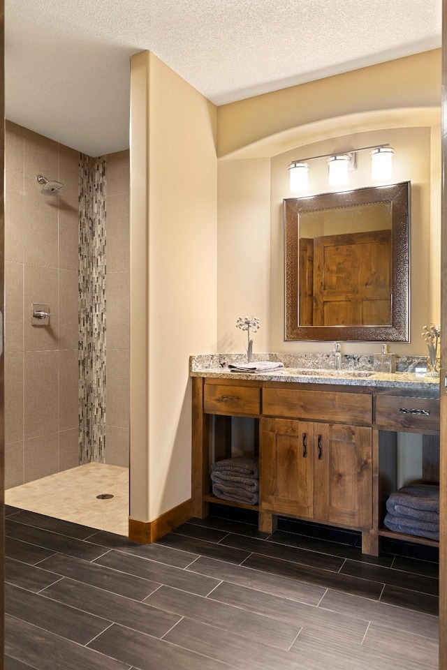 bathroom with tiled shower, a textured ceiling, and vanity