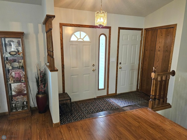 entryway with lofted ceiling, an inviting chandelier, and dark wood-type flooring