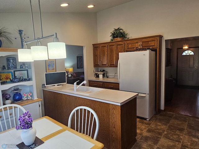 kitchen featuring sink, white fridge, decorative light fixtures, and a center island with sink