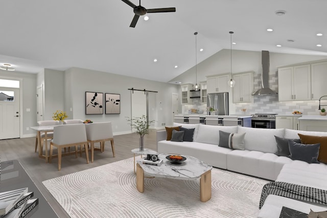 living room featuring a barn door, ceiling fan, light hardwood / wood-style flooring, and high vaulted ceiling