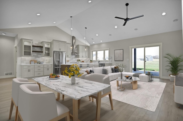 dining space with plenty of natural light, ceiling fan, high vaulted ceiling, and light hardwood / wood-style flooring