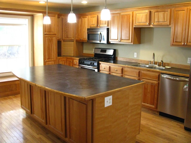 kitchen featuring light wood-type flooring, stainless steel appliances, sink, decorative light fixtures, and a center island