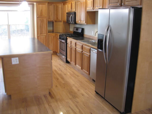 kitchen with pendant lighting, sink, light hardwood / wood-style flooring, a kitchen island, and stainless steel appliances